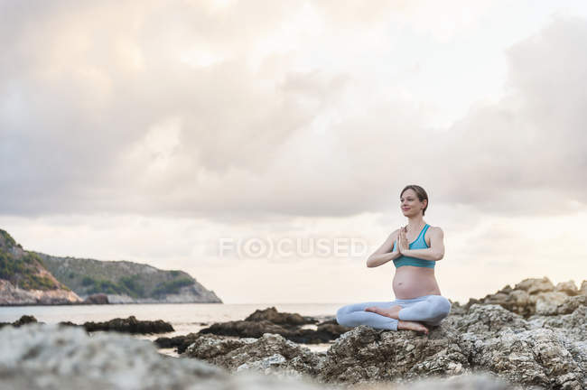 Беременная женщина практикует йогу в море — стоковое фото