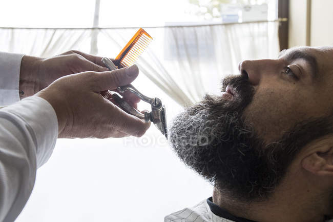 Парикмахерская стрижет бороду в парикмахерской — стоковое фото