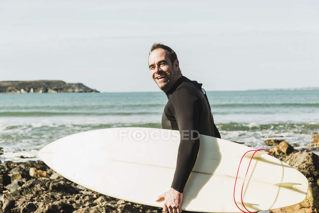 Francia, Bretagne, Finistere, Penisola di Crozon, uomo felice sulla spiaggia rocciosa con tavola da surf — Foto stock