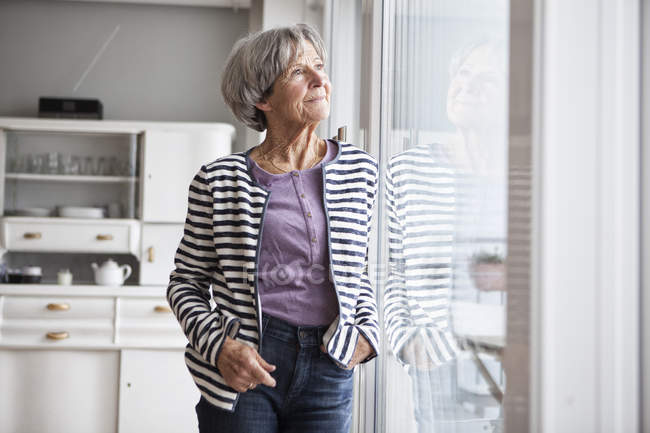Ritratto di donna anziana che guarda attraverso la finestra a casa — Foto stock