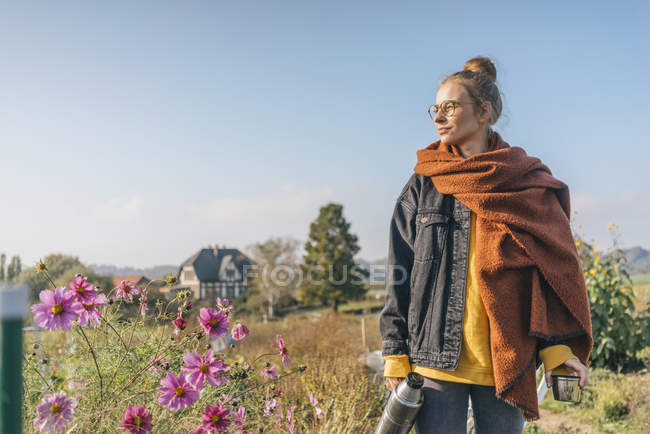 Jeune femme avec thermos flasque debout dans le jardin cottage — Photo de stock