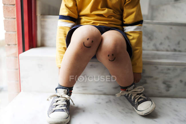 Menino sentado nas escadas com rostos sorridentes nos joelhos — Fotografia de Stock