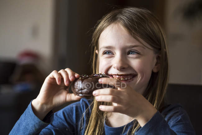 Portrait of smiling girl eating chocolate doughnut — Stock Photo