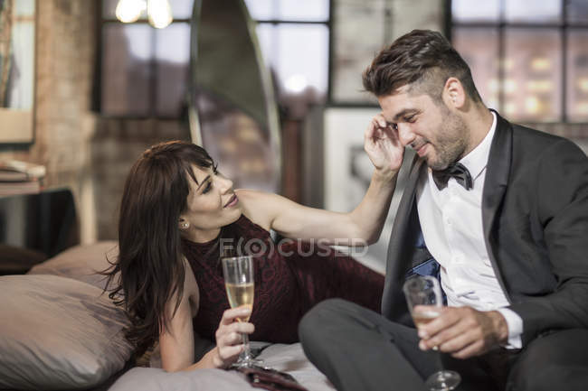 Smiling couple in elegant clothing drinking champagne in bed — Stock Photo