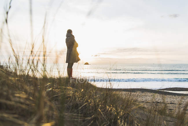 Mulher de pé na costa ao pôr do sol, França, Bretagne, Finistere, Península de Crozon — Fotografia de Stock