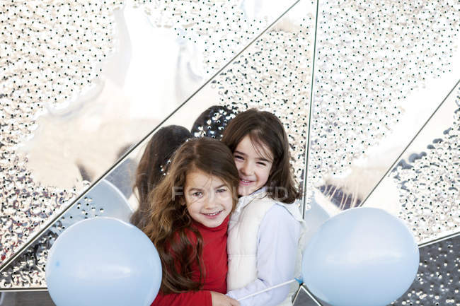 Due bambine con palloncini che si coccolano davanti al muro di metallo — Foto stock