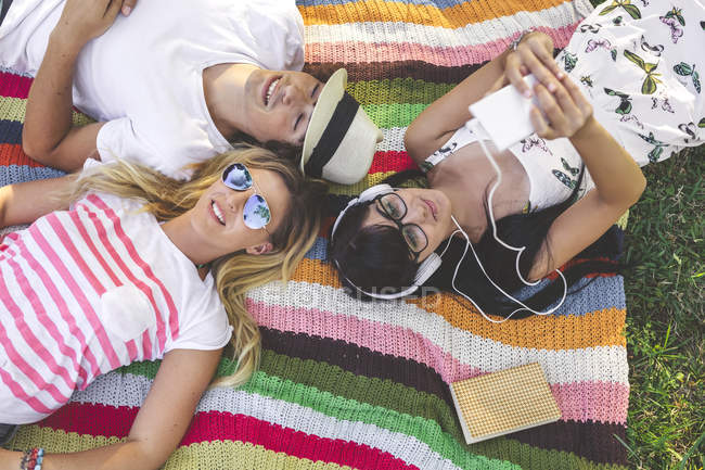 Jovem com amigos deitados no cobertor ouvindo música — Fotografia de Stock