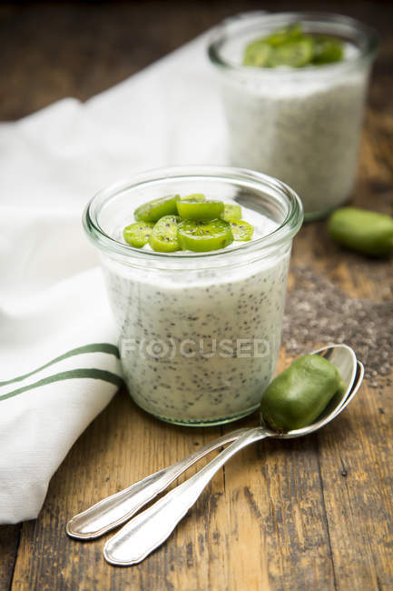 Glass of natural yoghurt with chia seeds and slices of kiwis on dark wood — Stock Photo