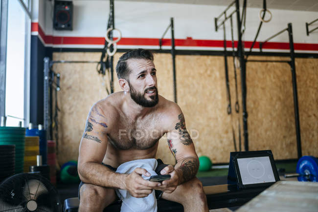Caucasien sportif homme reposant dans la salle de gym à l'aide de téléphone cellulaire — Photo de stock