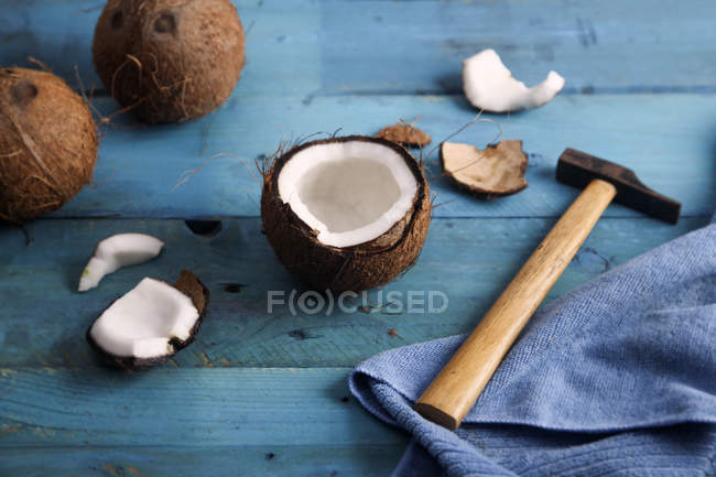 Apertura de coco con martillo sobre madera azul - foto de stock