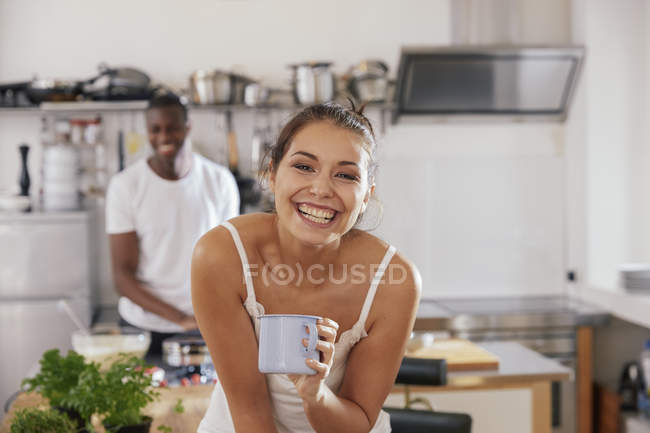 Портрет смішної молодої жінки з чашкою кави на кухні з хлопцем на фоні — стокове фото