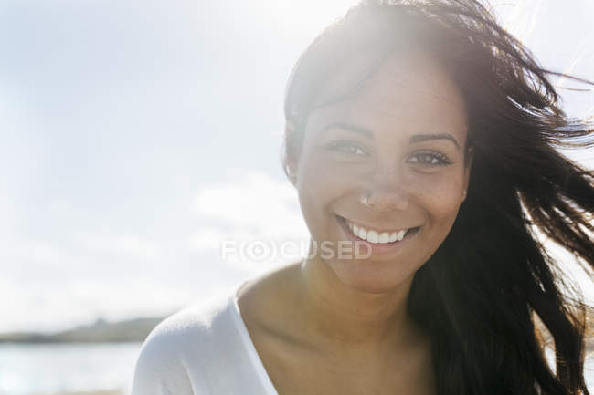 Retrato de sonriente nariz de mujer joven de pie a la luz de fondo - foto de stock