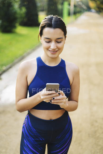 Mujer joven deportiva mirando el teléfono celular en el parque - foto de stock