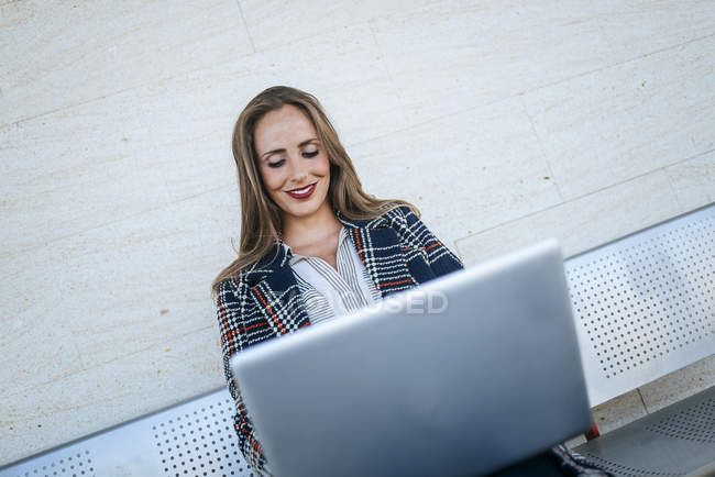 Бизнесмен, сидящая на скамейке и пользующаяся ноутбуком — стоковое фото
