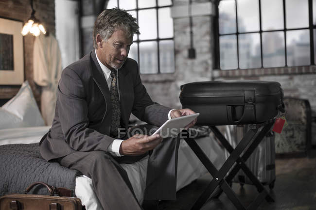 Mann sitzt im Hotelzimmer auf Bett und benutzt Tablet — Stockfoto