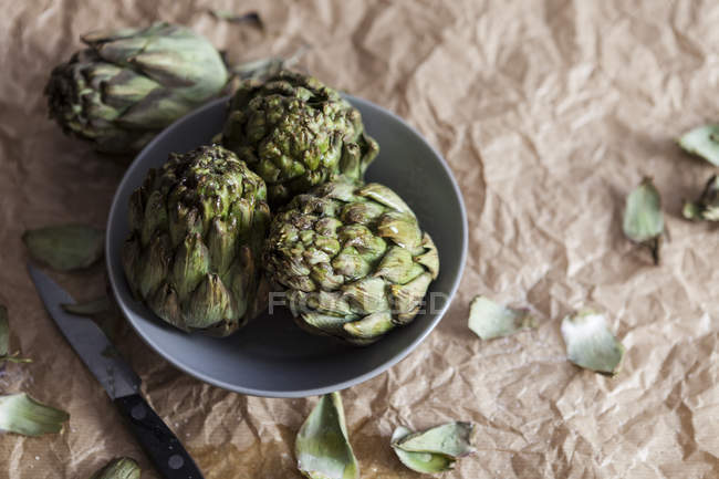 Three artichokes in a bowl on crumpled brown paper — Stock Photo