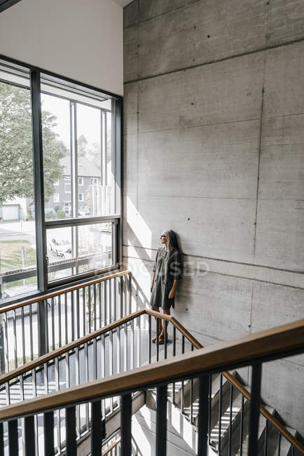 Frau mit langen grauen Haaren schaut aus Fenster im Treppenhaus — Stockfoto