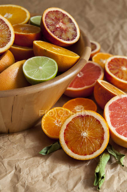 Wooden bowl of citrus fruits on crumpled brown paper — Stock Photo