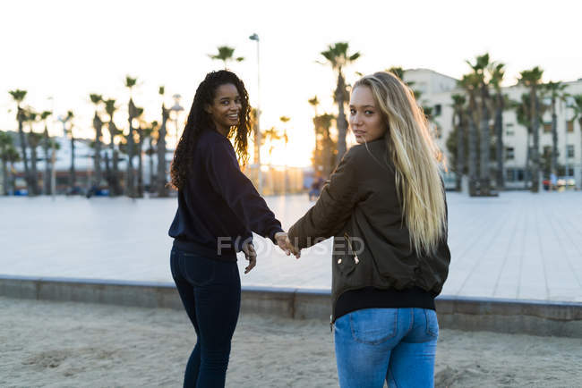 Zwei junge Frauen gehen Hand in Hand bei Sonnenuntergang — Stockfoto