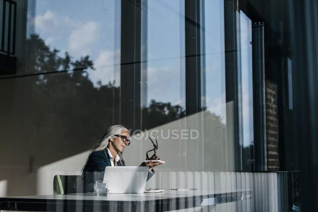 Geschäftsfrau sitzt am Schreibtisch und betrachtet Skulptur — Stockfoto