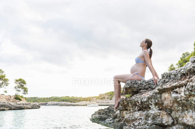 Pregnant woman sitting on rock at sea — Stock Photo