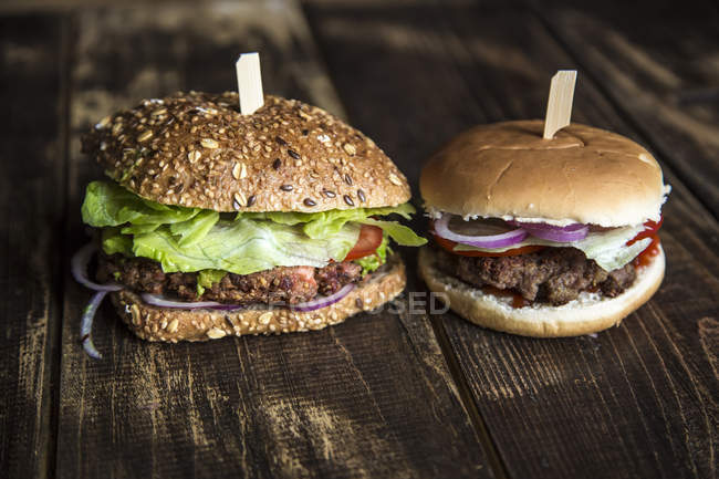 Burger végétarien avec galette de betteraves, crème d'avocat, salade et oignons à côté d'un hamburger avec boulette de viande à droite — Photo de stock