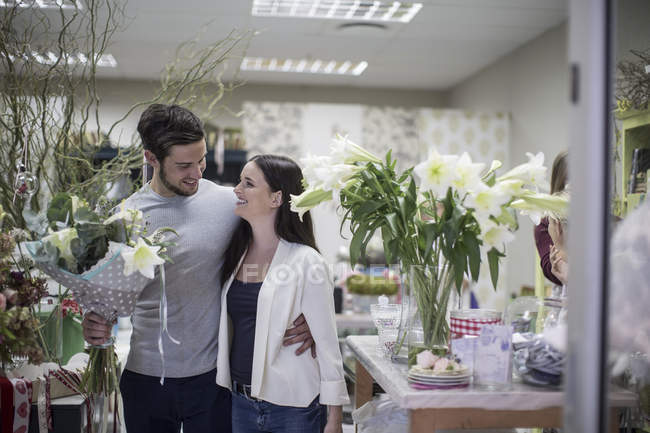 Happy young couple with bunch of flowers leaving flower shop — Stock Photo
