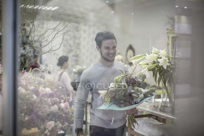 Smiling young man with bunch of flowers leaving flower shop — Stock Photo