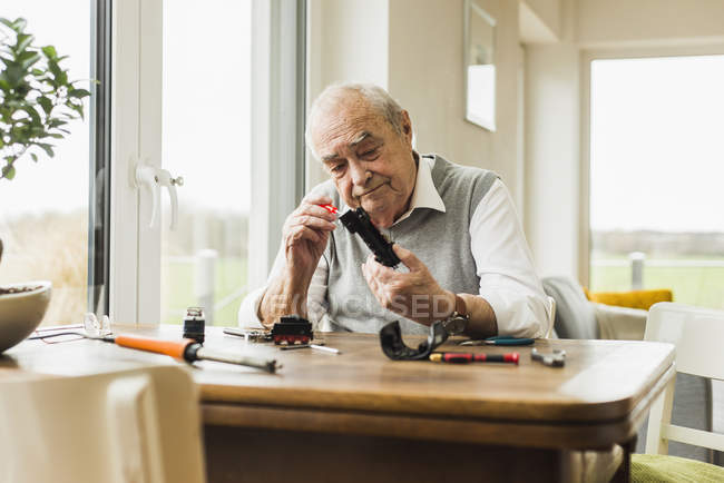 Hombre mayor reparando tren de juguete en casa — Stock Photo