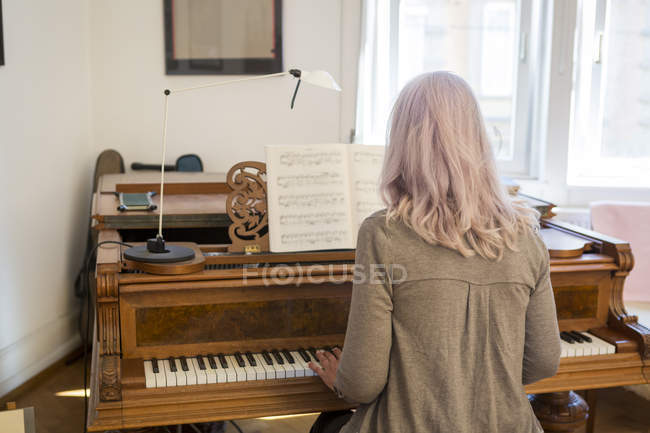 Vista posterior de la mujer mayor caucásica tocando el piano en casa - foto de stock