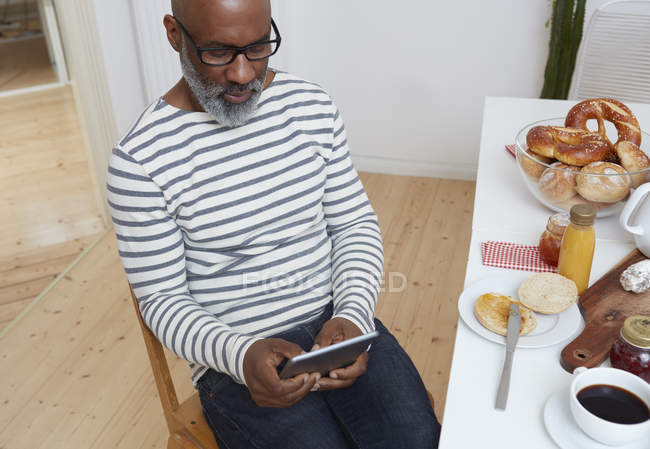 Uomo seduto al tavolo della colazione apparecchiato con tablet digitale — Foto stock