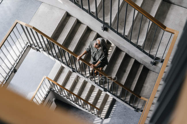 Frau mit langen grauen Haaren schaut aus Fenster im Treppenhaus — Stockfoto