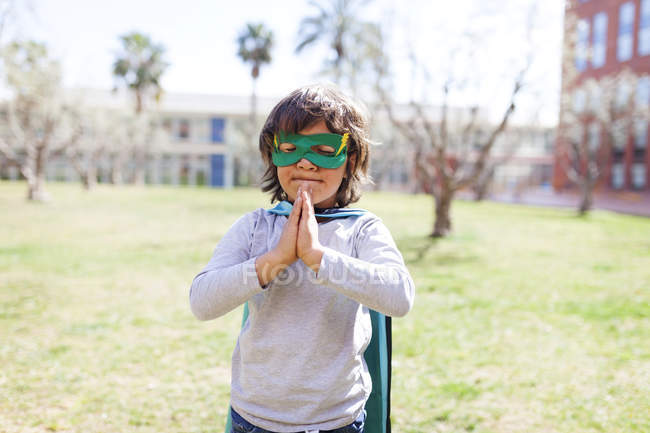 Portrait de petit garçon déguisé en super-héros debout sur une prairie — Photo de stock
