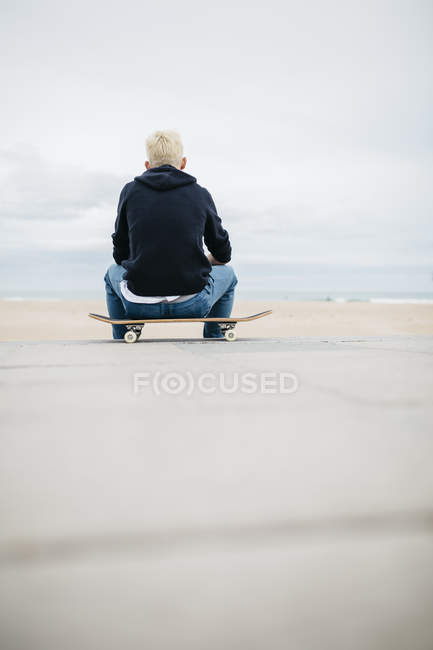 Молодой человек сидит на скейтборде — стоковое фото