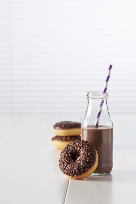 Garrafa de cacau e donuts com cobertura de chocolate — Fotografia de Stock