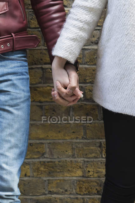 Close-up of couple hand in hand in front of brick wall — Stock Photo