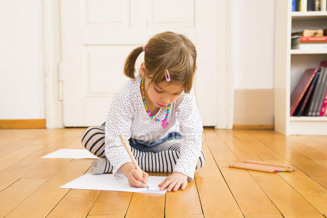 Fille assise sur le sol en bois et peinture avec crayon — Photo de stock