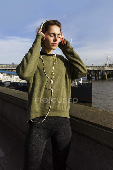 UK, London, female runner listening music at riverside — Stock Photo