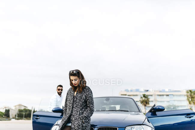 Young woman sitting on hood of car while boyfriend watching on background —  vehicle, outdoor - Stock Photo | #177536878