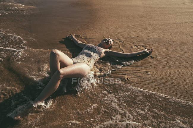 Brazil, Bahia, woman lying on wet sand at seafront — Stock Photo