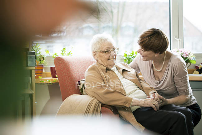Adult daughter talking to her mother with Alzheimer's disease in her room at retirement home — Stock Photo