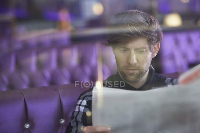Smiling young man sitting in a lounge bar reading newspaper — Stock Photo
