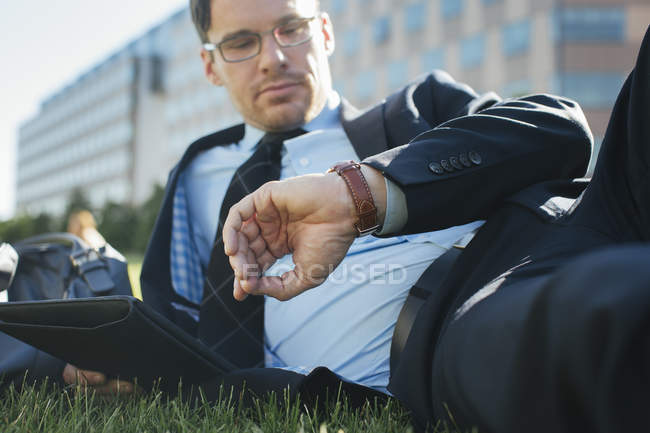 Businessman resting on meadow with digital tablet checking the time — Stock Photo