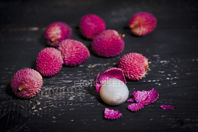Whole and peeled lychee on dark wood — Stock Photo