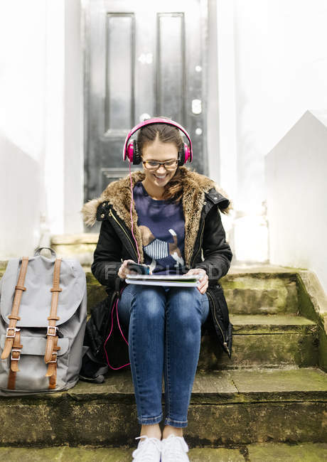 Student girl with headphones and writing pad sitting on stairs — Stock Photo