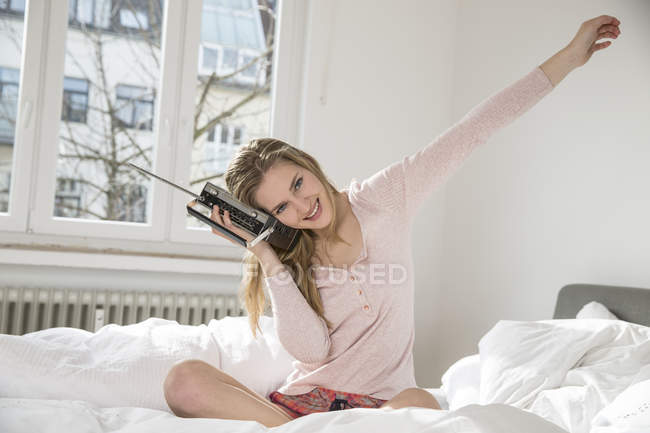 Портрет усміхнений молода жінка, сидячи на її ліжко прослуховування музики від радіо — стокове фото