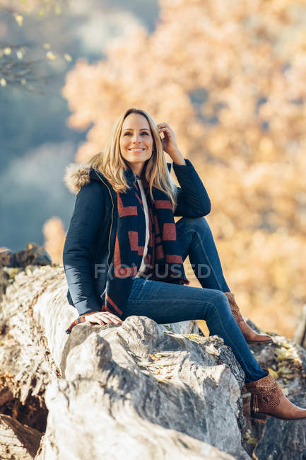 Lächelnde Frau sitzt auf Baumstamm und genießt den Herbst im Wald — Stockfoto