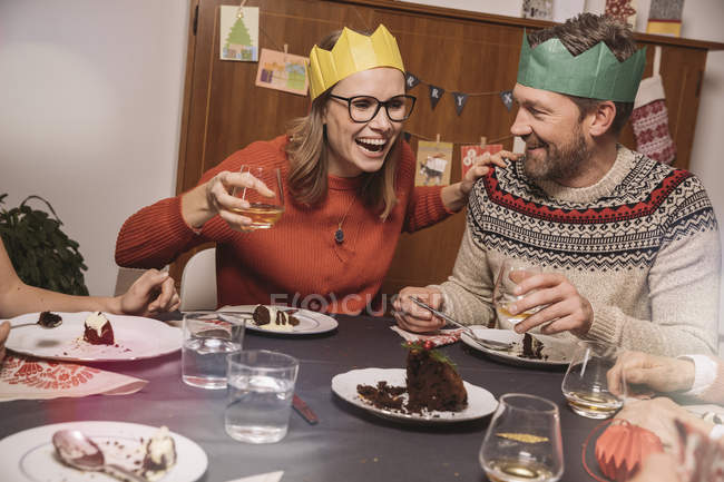 Coppia felice con corone di carta che ridono mentre cenano a Natale — Foto stock