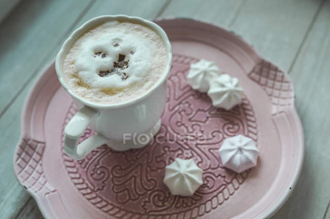 Cup of white coffee with chocolate shaving and meringues on a plate — Stock Photo