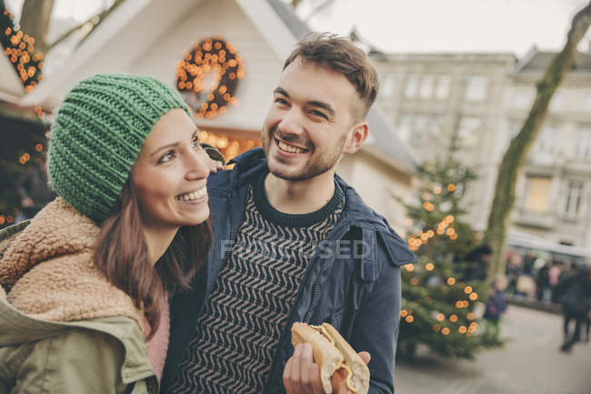 Happy couple having a snack on the Christmas Market — Stock Photo